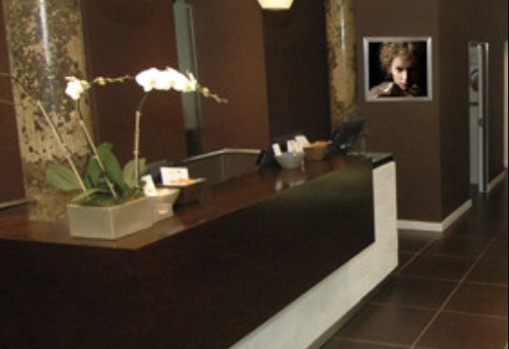 Modern reception area with a sleek desk, decorative plants, and a framed picture on the wall showcasing different hair styles. - Scott J Salons in New York, NY