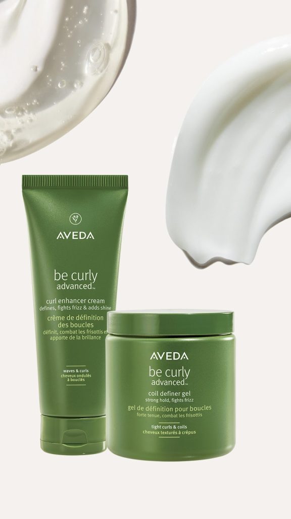 Aveda be curly styling cream tube and curl defining gel container displayed with artistic swatches of the products above them. - Scott J Salons in New York, NY