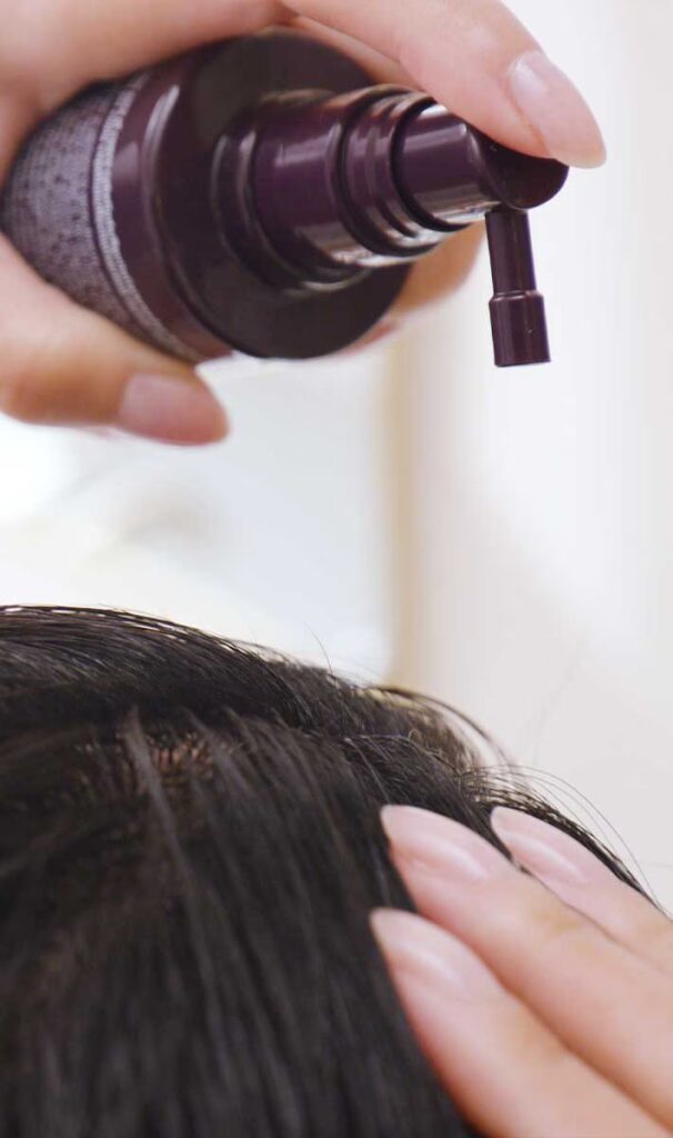 Hands applying hair care product from a pump bottle onto a person's scalp. - Scott J Salons in New York, NY