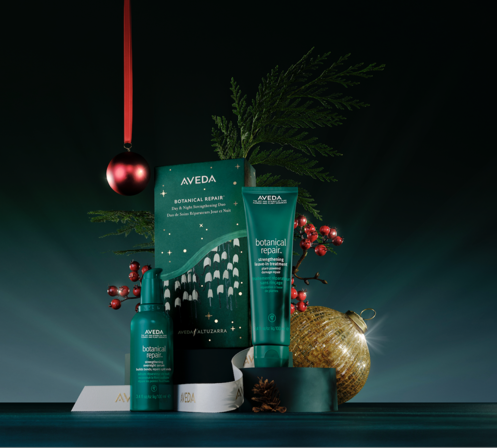 Aveda Botanical Repair holiday gift set with green packaging, a red bauble, and pine branches on display. - Scott J Salons in New York, NY