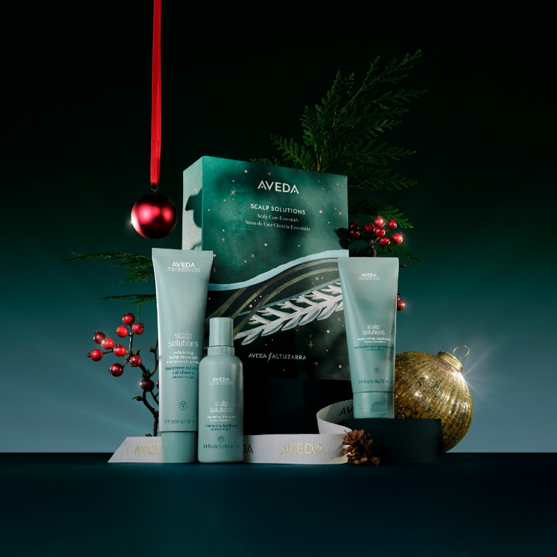 Aveda Scalp Solutions products displayed with festive decorations, including a red bauble and gold ornament against a dark background. - Scott J Salons in New York, NY