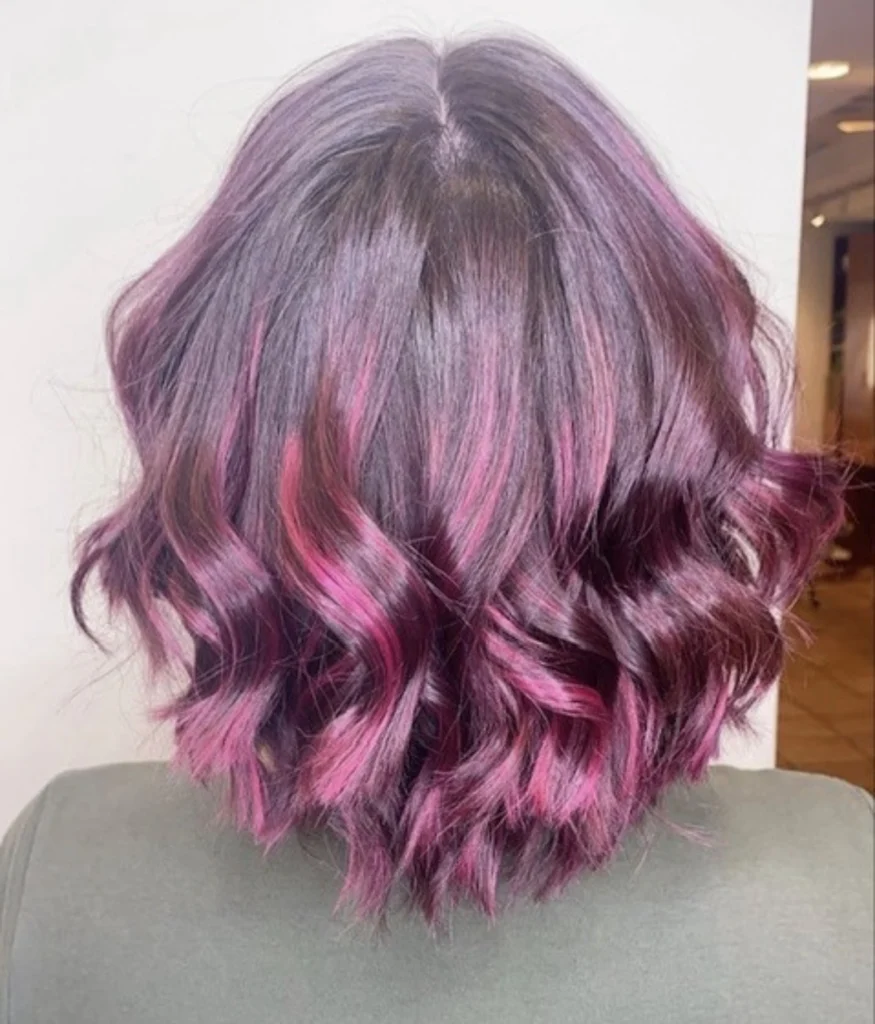 A person with short, wavy hair dyed dark purple with bright pink highlights is shown from the back, wearing a green top. - Scott J Salons in New York, NY