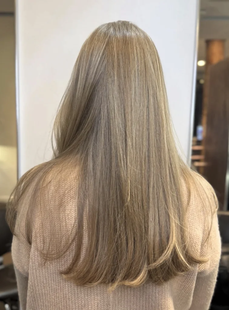 Person with long, straight, light brown hair wearing a beige sweater, shown from the back in an indoor setting. - Scott J Salons in New York, NY