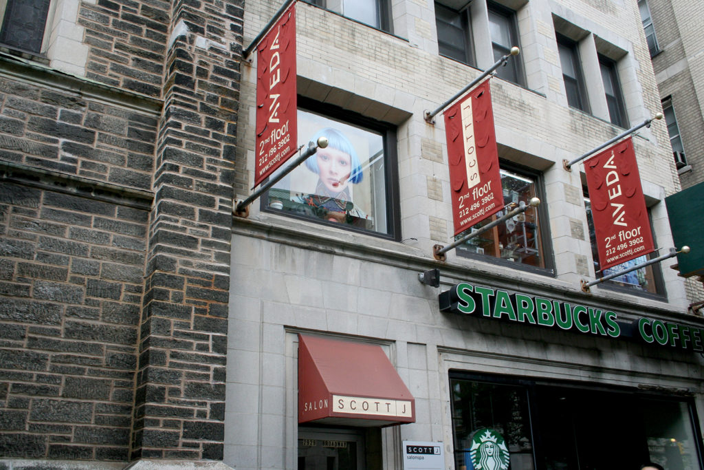Street-level view of a building with Starbucks Coffee on the ground floor and banners for Salon Scotti and NÉDA on the upper floors. - Scott J Salons in New York, NY