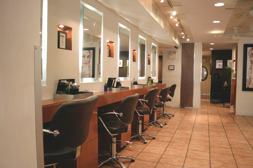 A modern hair salon interior with empty brown styling chairs, large mirrors, and tiled floor, brightly lit with overhead lights. - Scott J Salons in New York, NY
