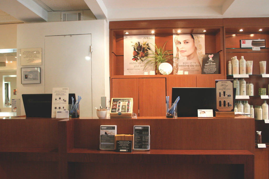 Reception desk at a salon or spa with product displays, promotional posters, and shelves stocked with hair and beauty products in the background. - Scott J Salons in New York, NY