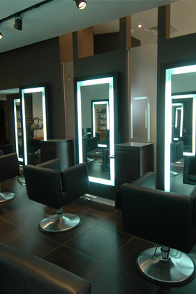 Modern hair salon interior with black styling chairs, illuminated mirrors, and dark tile flooring. - Scott J Salons in New York, NY